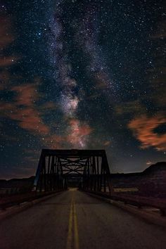 the night sky is filled with stars and clouds above a bridge that stretches into the distance