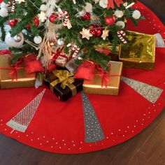 a christmas tree with presents under it on a red tableclothed place mat and wooden floor