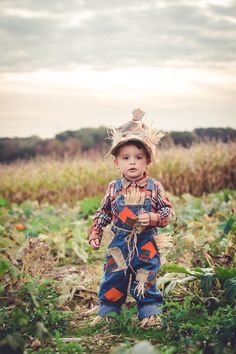 a little boy standing in the middle of a field wearing overalls and a cowboy hat