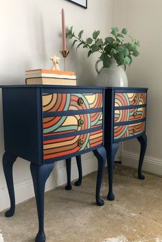 two colorful painted drawers next to a vase with a plant on top and books on the bottom