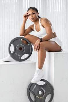 a woman sitting on top of a white block next to a barbell weight plate