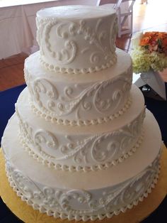 a three tiered white wedding cake sitting on top of a blue cloth covered table