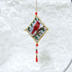 a cross stitch christmas ornament hanging on a white lace tablecloth with a red rose