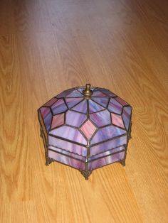 a small stained glass box sitting on top of a wooden floor next to a lamp