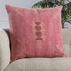 a pink pillow sitting on top of a couch next to a potted palm tree