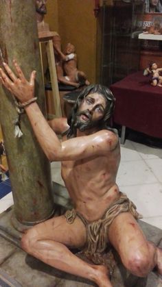 a statue of jesus nailed to a tree in a room with other figurines