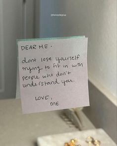 a note attached to a bathroom mirror with some gold beads on the counter and a toothbrush in front of it