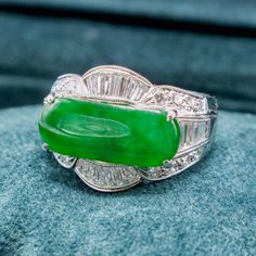 a green jade ring sitting on top of a blue stone covered surface with diamonds around it