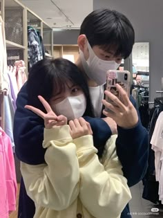 a man and woman wearing face masks in a clothing store looking at their cell phones