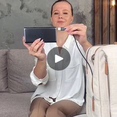 a woman sitting on a couch holding up a laptop computer next to a luggage bag