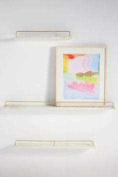 two white shelves with paintings on them against a wall, one is empty and the other has no shelfs