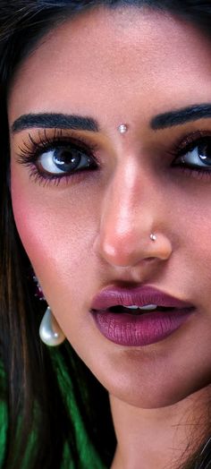 a close up of a woman with blue eyes and piercings on her nose looking at the camera