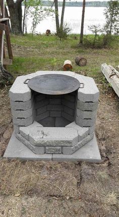 an outdoor fire pit in the middle of a field with trees and water behind it