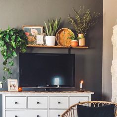 a living room with a large television on top of a white dresser next to a potted plant