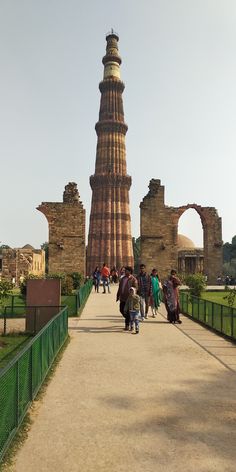 many people are walking on a path in front of a tall tower