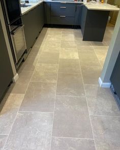 a kitchen with grey cabinets and tile flooring in the middle, along with stainless steel appliances