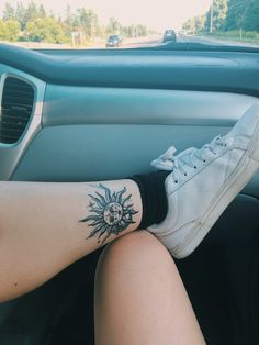 a woman's foot with a sun tattoo sitting in the passenger seat of a car