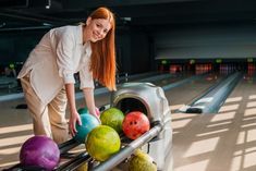 a woman leaning over a rail to pick up some bowling balls