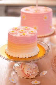 two pink and yellow cakes sitting on top of a table next to eachother