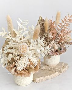 two vases filled with flowers on top of a stone slab next to each other