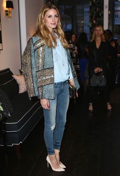 a woman standing in front of a couch wearing blue jeans and a jacket with sequins on it