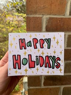 a hand holding up a card with the words happy holidays on it in front of a brick wall