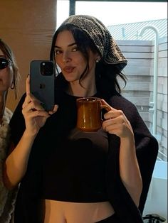 two women holding up their cell phones and coffee mugs in front of the camera