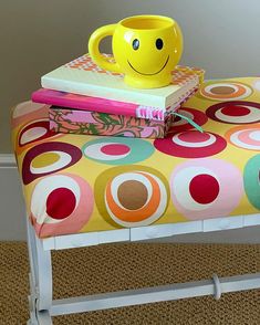 a yellow mug sitting on top of a colorful bench next to a stack of books