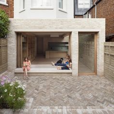 three people sitting on the ground in front of a brick building with an open door