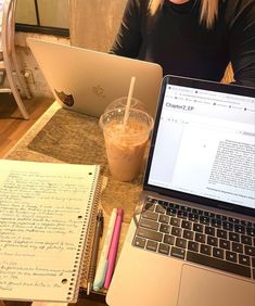 a woman sitting at a table with two laptops and a notepad in front of her