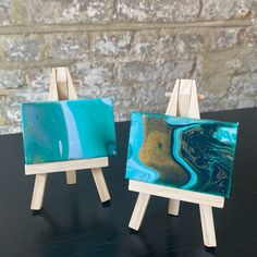 two wooden easels with paintings on them sitting on a table