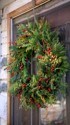 a wreath hanging on the front door of a house with red berries and pine cones