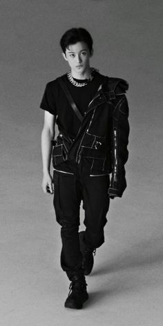 a young man is walking down the runway wearing all black clothing and shoes with chains on his neck