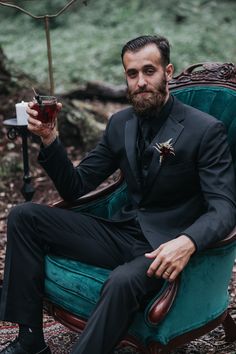 a man in a tuxedo holding a drink and sitting on a green chair