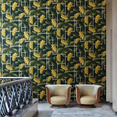 two chairs sitting next to each other in front of a wall with yellow leaves on it