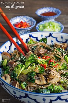 a bowl filled with broccoli, mushrooms and other vegetables next to chopsticks