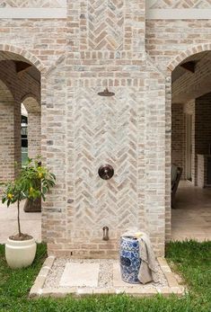 an outdoor shower in the middle of a brick building with two potted plants next to it