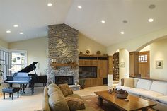 a living room filled with furniture and a piano in front of a fire place surrounded by windows