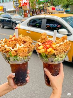 two people holding up cups filled with food on the side of a road next to a taxi