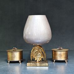 a white vase sitting on top of a table next to two gold containers and a silver container