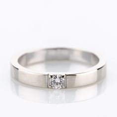 a white gold ring with a single diamond in the center, on a white background