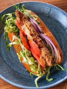 a sandwich with meat, tomatoes and lettuce on a blue plate sitting on a wooden table