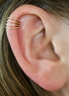 a close up of a person's ear with three thin gold rings on it