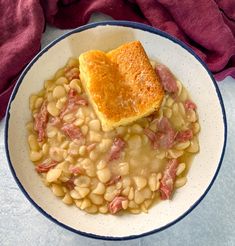 a white bowl filled with beans and ham on top of a blue rimmed plate