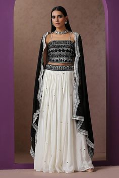 White lehenga with black Kashmiri aari placement embroidery. Paired with square neck embroidered blouse and black dupatta.
Components: 3
Pattern: Embroidery
Type Of Work: Kashmiri aari
Neckline: Square neck
Sleeve Type: Sleeveless
Fabric: Crepe, Georgette, Lining: Cotton
Color: White
Other Details: 
Lehenga:
Embroidered waistband
Length: 40 inches
Approx. weight: 2 kgs
Blouse:
Noodle strap on shoulder sleeve
Dupatta:
Cutwork embroidered borders
Model height: 5ft 7inches, wearing size S
Occasion: Traditional Black Palazzo Set For Reception, Elegant Georgette Lehenga With Motifs, Wedding Lehenga With Motifs In Black, White Anarkali Choli With Motifs, Anarkali Style White Choli With Motifs, White Choli With Motifs, White Sharara With Motifs For Navratri, Fitted White Lehenga With Motifs, White Fitted Lehenga With Motifs