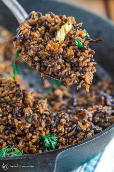 a spoon full of rice and herbs being lifted from a skillet with a fork