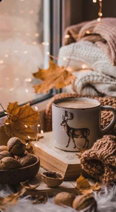 a cup of coffee sitting on top of a wooden table next to nuts and leaves