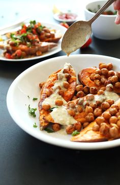 a white plate topped with meat covered in sauce next to bowls of beans and veggies