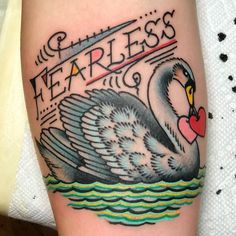 a black swan with a heart in its beak on the arm that says fearless and is surrounded by water