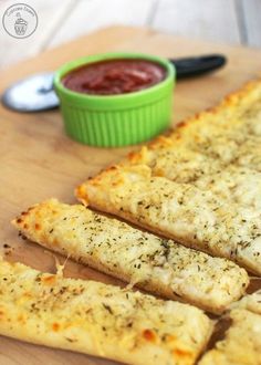 cheesy bread sticks with ketchup and dipping sauce on a cutting board